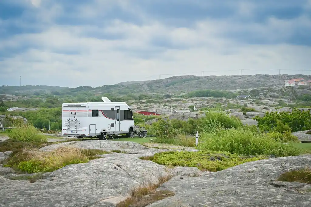 Vit husbil parkerad vid klippor och kustlandskap under blågrå himmel
