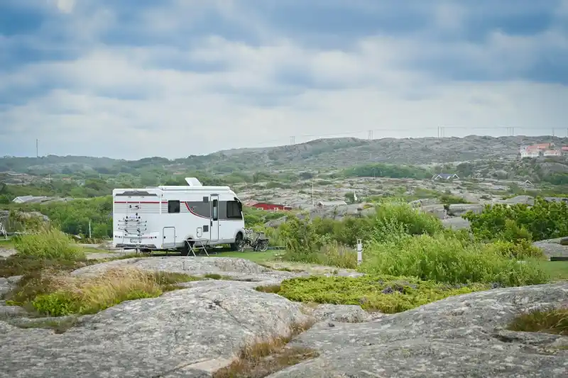 Vit husbil parkerad vid klippor och kustlandskap under blågrå himmel