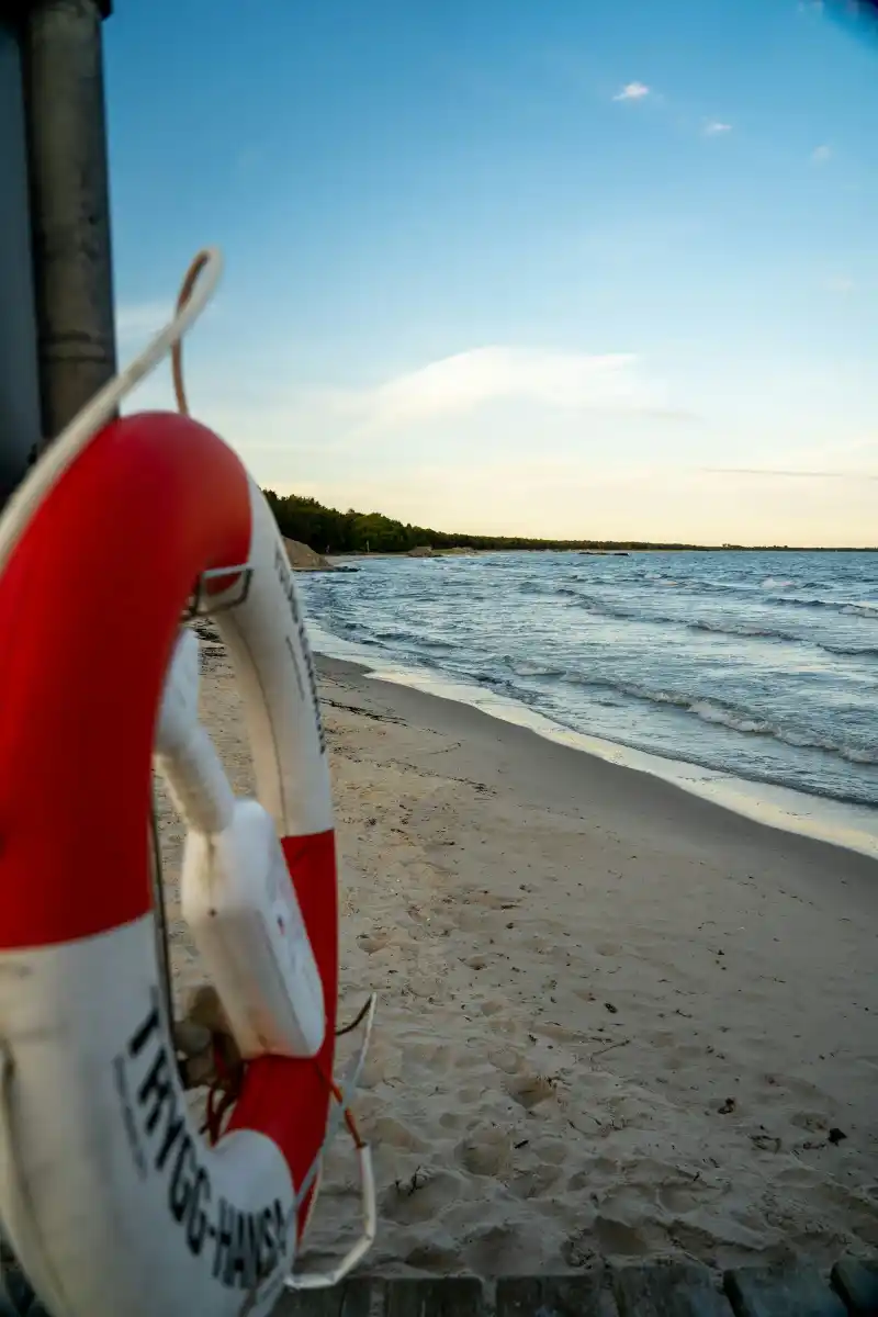 Rödvit livboj vid en sandstrand med hav och blå himmel i bakgrunden