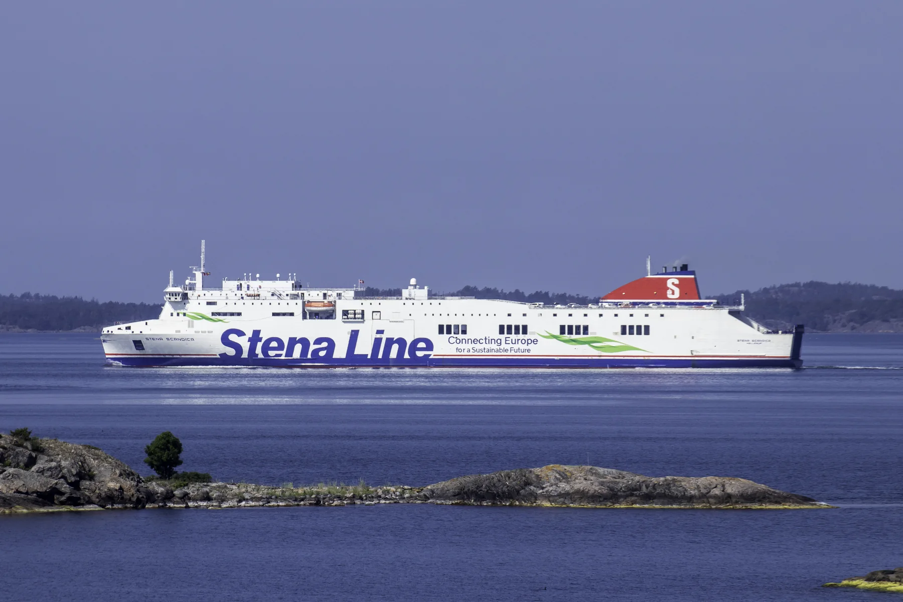 Stena Scandica sedd från sidan på blått vatten, med låga klippor i förgrunden.