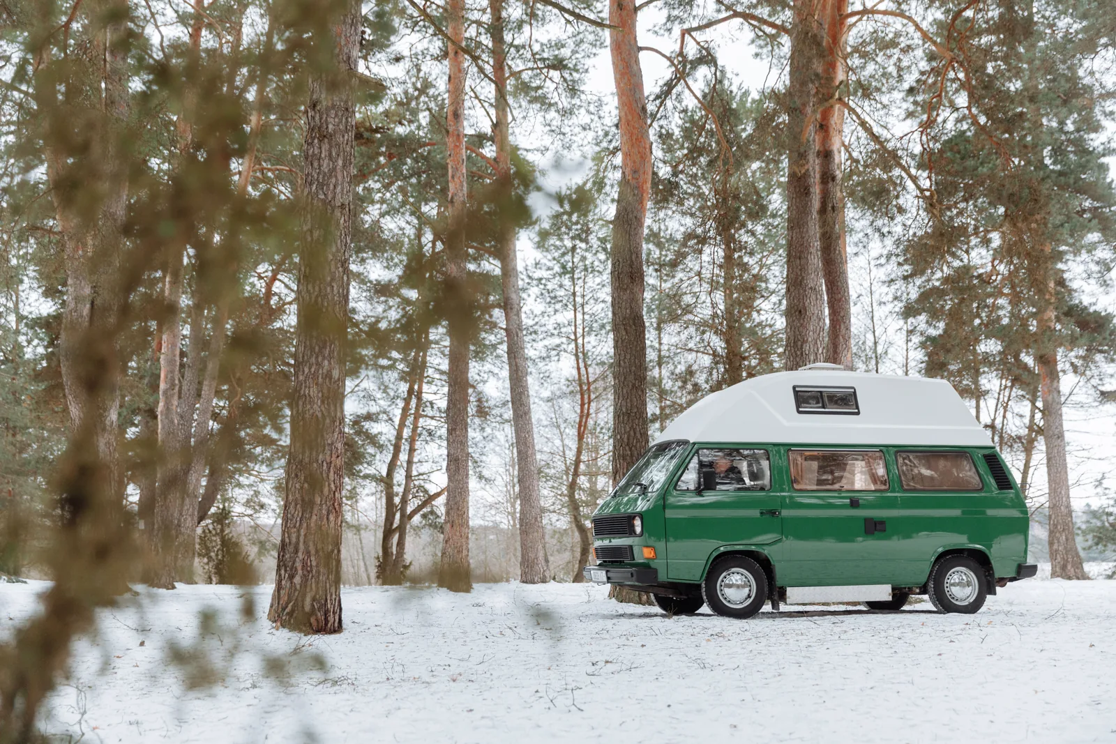 Grön campervan på en snötäckt väg bland träd.